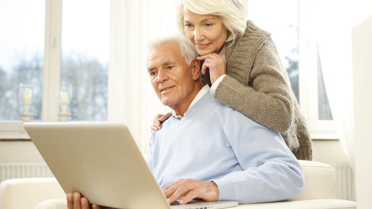 Paar sitzt auf einer Couch und schaut gemeinsam auf einen Laptop in einem hellen Raum.